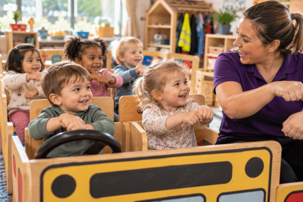 Toddlers sitting in a pretend bus rolling their arms to a favourite nursery song