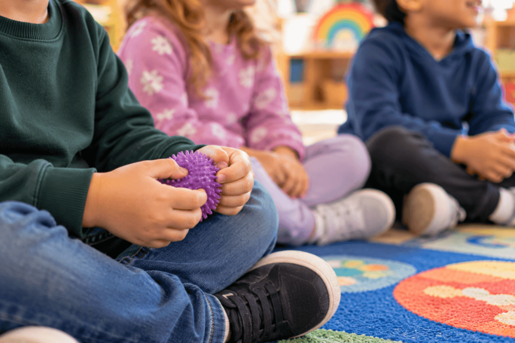 A child's hands holding a soft fidget toy during carpet time in an inclusive classroom